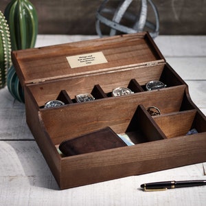 May include: A wooden box with a hinged lid, divided into compartments. The box contains several watches, a wallet, and a pen. The lid has a small plaque with the text "Things and  have accumulated  but memories last forever".