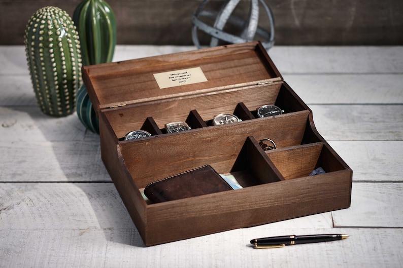 May include: A wooden box with a hinged lid, divided into compartments. The box contains several watches, a wallet, and a pen. The lid has a small plaque with the text "Things and  have accumulated  but memories last forever".