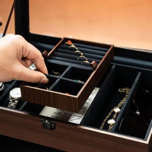 以下が含まれることがあります： 黒いベルベットで裏打ちされた複数のコンパートメントを備えた、暗い仕上げの木製ジュエリーボックス。 上部のトレイが持ち上げられ、指輪やその他のジュエリーが表示されます。 時計とサングラスも表示されます。