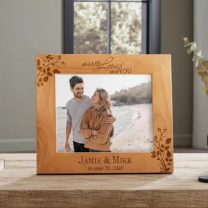 May include: A light brown wooden picture frame with the words "all of ME Loves all of YOU" engraved at the top. The frame has a photo of a couple on a beach. The bottom of the frame reads "Jamie & Mike October 20, 2020".