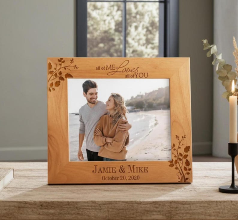 May include: A light brown wooden picture frame with the words "all of ME Loves all of YOU" engraved at the top. The frame has a photo of a couple on a beach. The bottom of the frame reads "Jamie & Mike October 20, 2020".