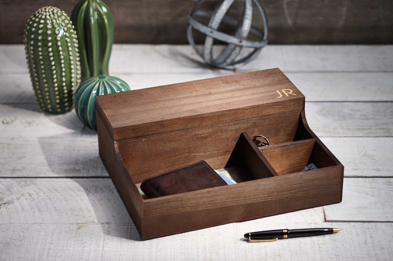 May include: A wooden box with compartments for organizing small items. The box has a lid with the initials "JR" engraved on it. The box is open and a brown leather wallet is inside.