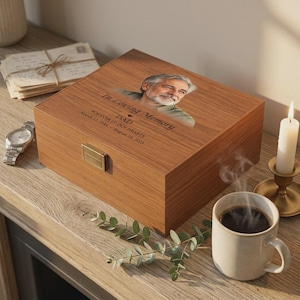 May include: A rectangular wooden keepsake box with a gold-tone metal latch. The lid features a printed portrait of a man, the text In Loving Memory DAD FOREVER IN OUR HEARTS, and the dates March 12, 1954 - August 28, 2023.