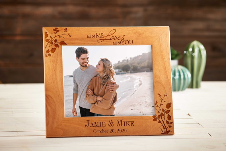 May include: A light brown wooden picture frame with the words "all of ME Loves all of YOU" engraved at the top. The frame has a photo of a couple on a beach. The names "Jamie & Mike" and the date "October 20, 2020" are engraved at the bottom.