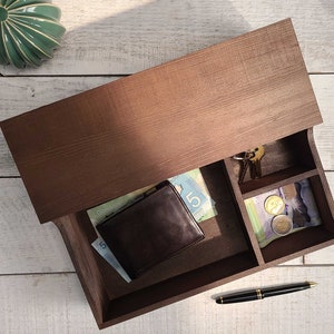 May include: A brown wooden box with a drawer that is open. The drawer contains a brown leather wallet, Canadian bills, a pen, and a small compartment with coins.