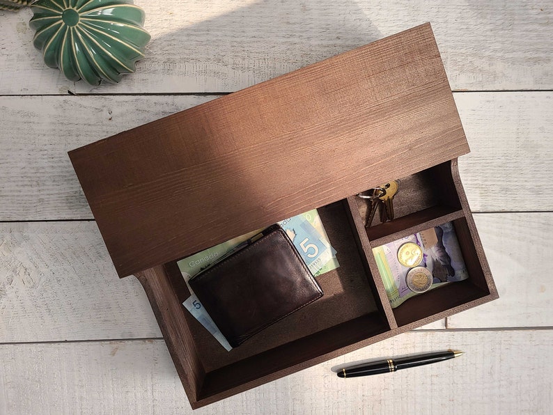 May include: A brown wooden box with a drawer that is open. The drawer contains a brown leather wallet, Canadian bills, a pen, and a small compartment with coins.