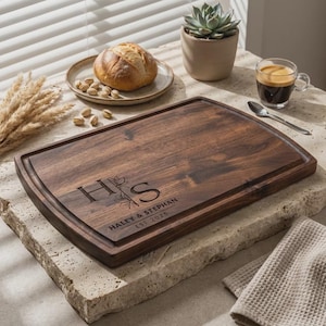 May include: A rectangular wooden chopping board with a dark brown finish. The board has a carved groove around the edge and engraved initials "H S" with the names "Haley & Stephan" and the year "EST 2025".