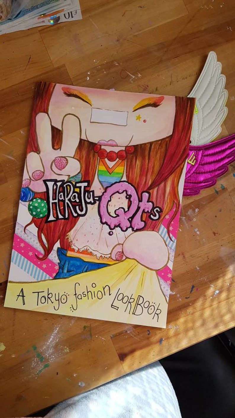 May include: A book cover with a cartoon illustration of a girl with red hair wearing a rainbow shirt and blue jeans. The title of the book is "Harajuku QTs" and the subtitle is "A Tokyo fashion lookbook".