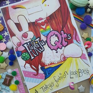 May include: A colorful book cover with a cartoon illustration of a girl with red hair and a peace sign. The book title is "Harajuku QTs" and the subtitle is "A Tokyo fashion LookBook".