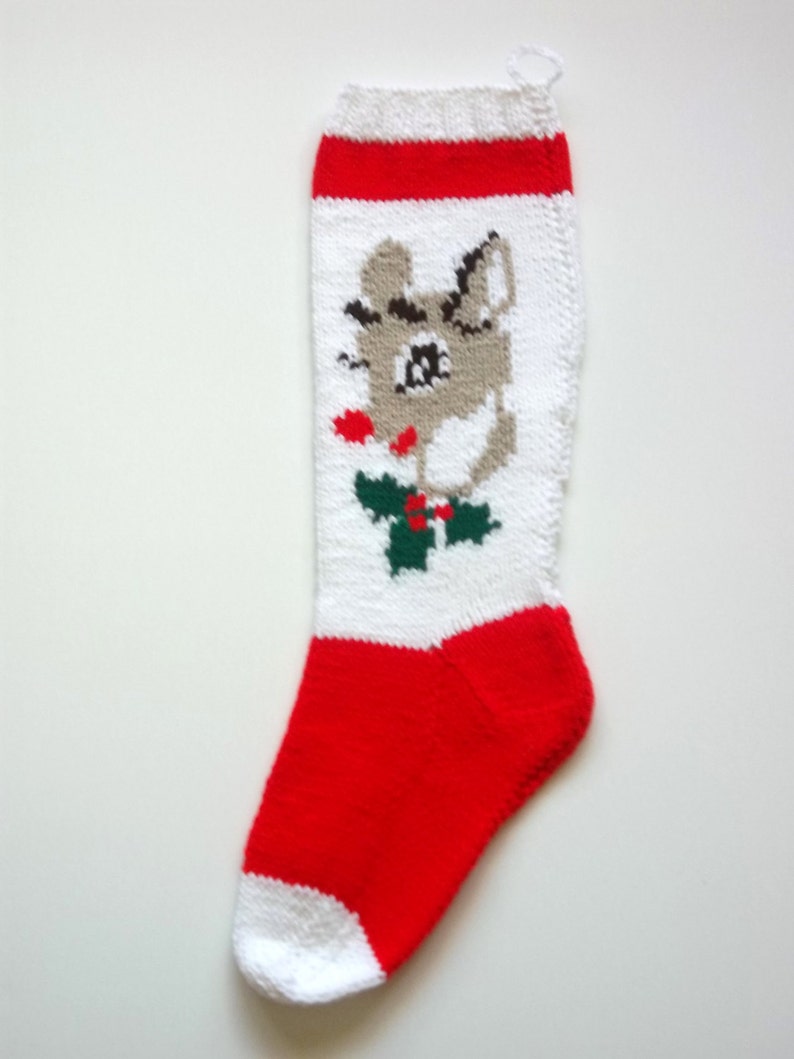 May include: White and red knitted Christmas stocking with a cartoon reindeer design. The reindeer is gray with a red nose and green holly.