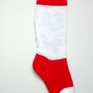 May include: A white knitted stocking with a red band at the top and a red toe. The stocking has a loop at the top for hanging.
