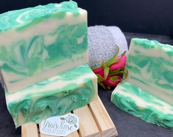 May include: Three bars of handmade soap with a green and white swirl pattern. The soap is on a wooden soap dish with a sticker that says "Yrais Rose Creations".