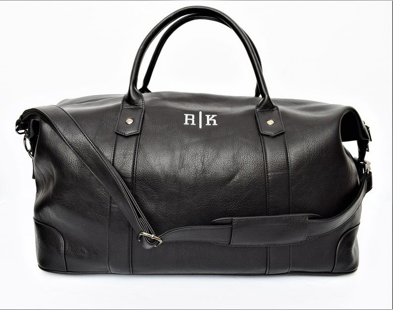 May include: Black leather duffel bag with a shoulder strap and top handles. The bag has a monogrammed "R|K" on the front.