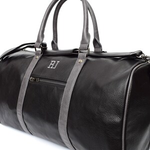 Pu&ograve; includere: Borsa da viaggio in pelle nera con finiture in pelle grigia e una tasca con cerniera. La borsa ha un monogramma "RJ" sul davanti.