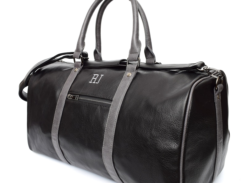 Pu&ograve; includere: Borsa da viaggio in pelle nera con finiture in pelle grigia e una tasca con cerniera. La borsa ha un monogramma "RJ" sul davanti.