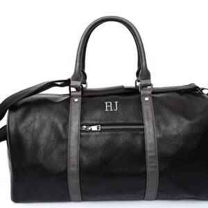 Pu&ograve; includere: Borsa da viaggio in pelle nera con finiture in pelle grigia e chiusura a zip. La borsa ha una maniglia superiore e una tracolla. Le iniziali "RJ" sono ricamate sul davanti della borsa.