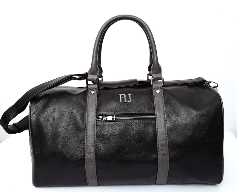 Pu&ograve; includere: Borsa da viaggio in pelle nera con finiture in pelle grigia e chiusura a zip. La borsa ha una maniglia superiore e una tracolla. Le iniziali "RJ" sono ricamate sul davanti della borsa.