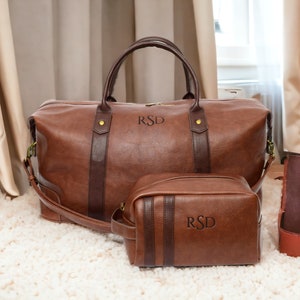 May include: Two brown leather travel bags with the initials "RSD" embossed on them. The larger bag has a top handle and a shoulder strap. The smaller bag is a toiletry bag.