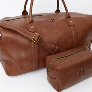 May include: A brown leather travel duffel bag with a matching brown leather toiletry bag. Both bags have a gold zipper and the initials "C|D" are embossed on the front.