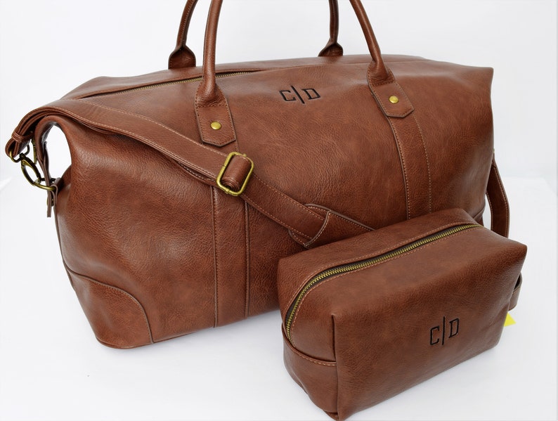 May include: A brown leather travel duffel bag with a matching brown leather toiletry bag. Both bags have a gold zipper and the initials "C|D" are embossed on the front.