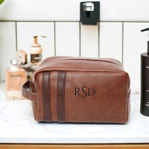 May include: Brown leather travel toiletry bag with a zipper closure and a top handle. The bag has a brown leather strap with the initials "RSD" embossed on it.