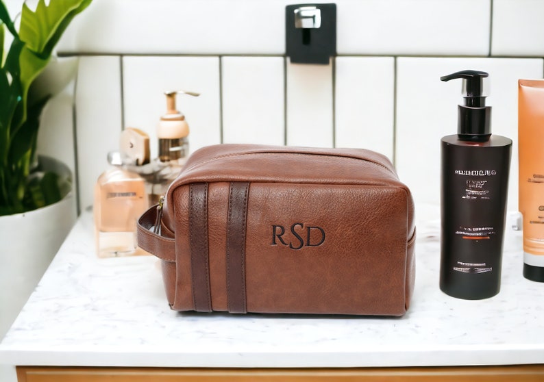 May include: Brown leather travel toiletry bag with a zipper closure and a top handle. The bag has a brown leather strap with the initials "RSD" embossed on it.