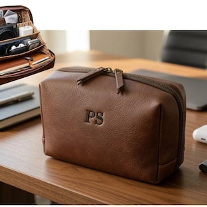 May include: A brown leather-textured zippered pouch featuring the embossed letters PS on the front. The interior is lined with a striped fabric and contains multiple compartments organized with various electronic accessories, cables, and a notebook.