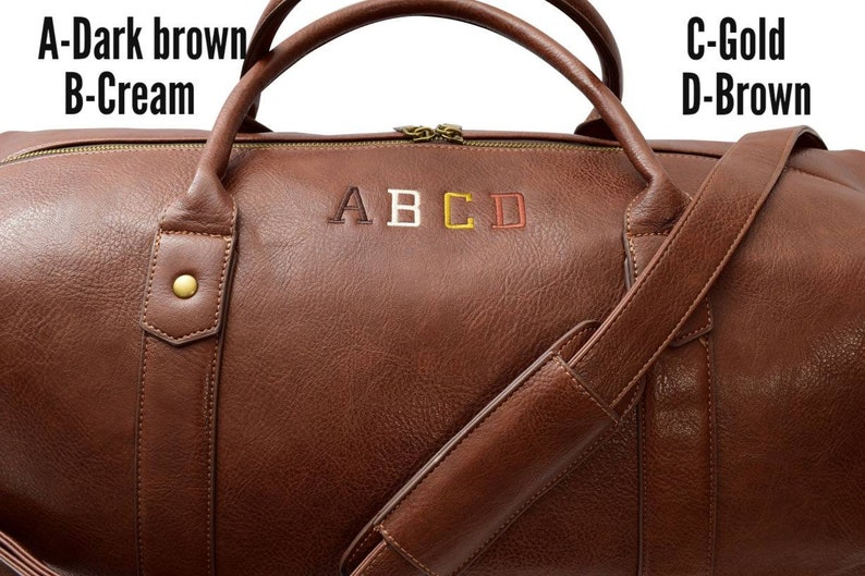 Pu&ograve; includere: Una borsa da viaggio in pelle marrone con una tracolla. La borsa ha una chiusura a zip ed &egrave; monogrammata con le lettere A, B, C e D in diversi colori. Le lettere sono ricamate in marrone scuro, crema, oro e marrone.