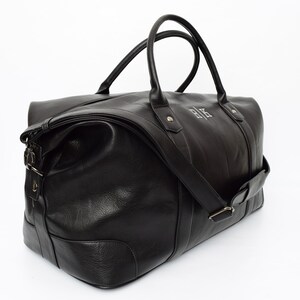 May include: A black leather duffel bag with a top handle and a shoulder strap. The bag has a zipper closure and a monogrammed "R.K." on the front.