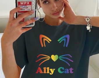 Puede incluir: Camiseta negra con un gráfico de gato arcoíris y el texto "Ally Cat". El texto "Size Up For Trendy Oversized Look" está en la parte inferior de la imagen.