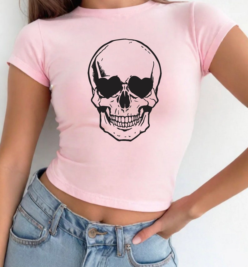 May include: A pink cropped t-shirt with a black skull graphic wearing sunglasses. The skull has a toothy grin.