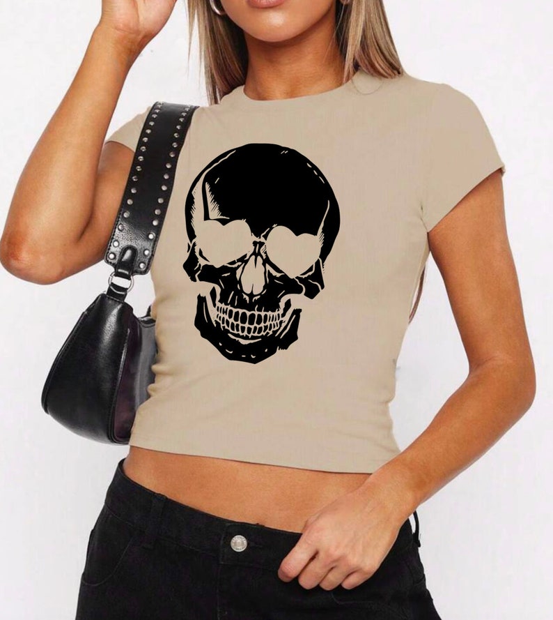 May include: A beige cropped t-shirt with a black skull graphic wearing sunglasses.