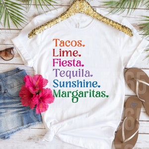 以下が含まれることがあります： レインボーカラーで「Tacos. Lime. Fiesta. Tequila. Sunshine. Margaritas.」とプリントされた白いTシャツです。