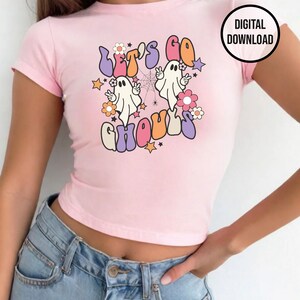 May include: A pale pink crop top with the words "Let's Go Ghouls" in a retro style, with cartoon ghosts, flowers, and stars. The top has short sleeves and a fitted shape. A "DIGITAL DOWNLOAD" graphic is in the upper right corner.