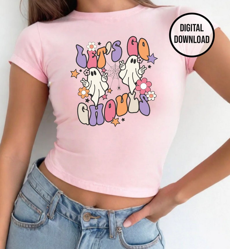 May include: A pale pink crop top with the words "Let's Go Ghouls" in a retro style, with cartoon ghosts, flowers, and stars. The top has short sleeves and a fitted shape. A "DIGITAL DOWNLOAD" graphic is in the upper right corner.