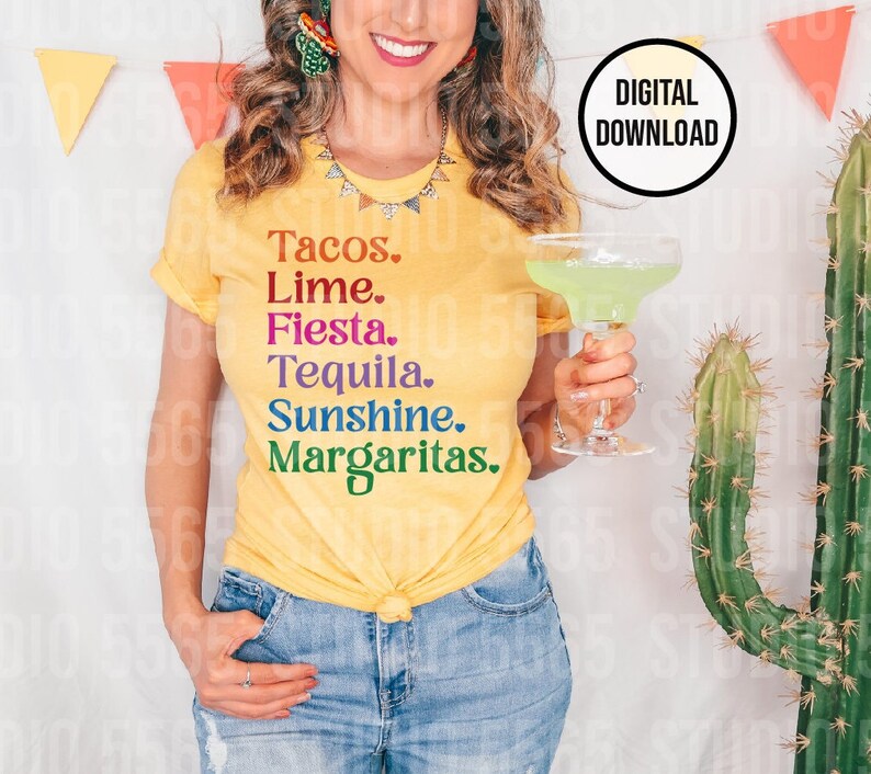 以下が含まれることがあります： 「Tacos. Lime. Fiesta. Tequila. Sunshine. Margaritas.」と虹色の文字がプリントされた黄色のTシャツ。女性がTシャツを着て、透明なグラスにマルガリータを持っている。