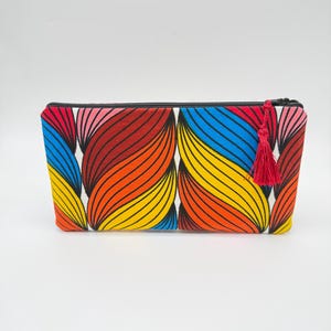 May include: A rectangular cosmetic bag with a vibrant, abstract pattern of curved lines in red, orange, yellow, and blue. The bag has a black zipper and a red tassel attached to the zipper pull. The background is plain white.