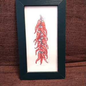 Könnte beinhalten: Eine gerahmte Illustration eines Bündels roter Chilischoten, die an einer Schnur hängen. Die Illustration ist in Schwarzweiß mit roten Akzenten. Der Rahmen ist dunkelgrün.