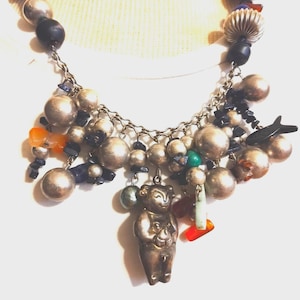 Könnte beinhalten: Eine silberne Halskette mit verschiedenen Perlen, darunter silberne, schwarze, blaue, grüne, orangefarbene und rote. Die Halskette hat einen silbernen Anhänger in Form eines Bären.