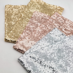 May include: Four fabric swatches in gold, rose gold, and silver, each covered in shimmering sequins. The swatches are arranged diagonally, showcasing the different colors and textures. Ideal for crafting or event decor.