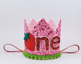 May include: Pink felt crown with green glitter trim and a red felt strawberry. The crown says "one" in red glitter letters.