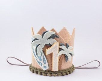 May include: A felt crown with a brown base, a white number one, and blue and green palm trees. The crown has a green pom-pom trim and a brown tie.