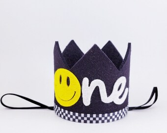 May include: A black felt crown with a white felt "one" and a yellow smiley face. The crown has a black and white checkered ribbon.