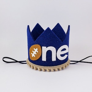 May include: Blue felt crown with a white felt "one" and a brown felt football. The crown has a tan felt trim with tan pom-poms.