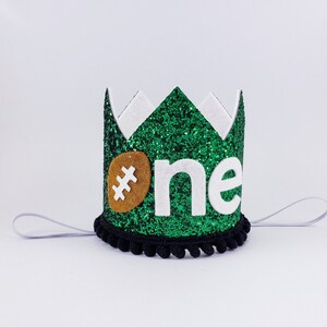 May include: Green glitter crown with a white felt 'one' and a brown felt football. The crown has a black elastic band.
