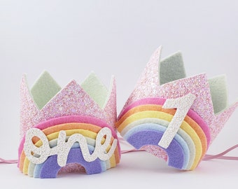 May include: Two pink glitter felt crowns with rainbow felt accents. One crown says "one" and the other has the number "1" on it.