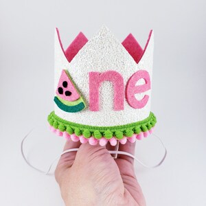 May include: White felt crown with pink felt trim and a watermelon design. The crown says "one" in pink felt letters and has a green and pink pom-pom trim.