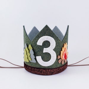 May include: A green felt crown with a white felt number 3, a felt campfire, and felt pine trees. The crown has a brown felt band.