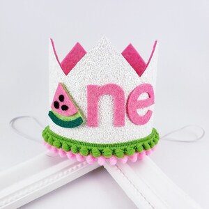 May include: White felt crown with pink felt trim and a pink felt "one" with a green and red felt watermelon slice on the side. The crown has a green and pink pom-pom trim.