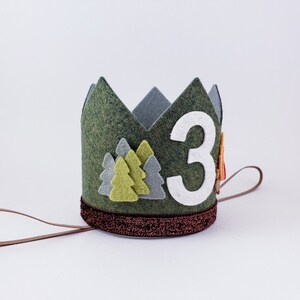 May include: Green felt crown with a white felt number 3, green and gray felt trees, and a brown felt tie.